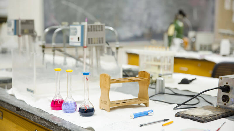 beakers on a lab table containing liquids of various colors