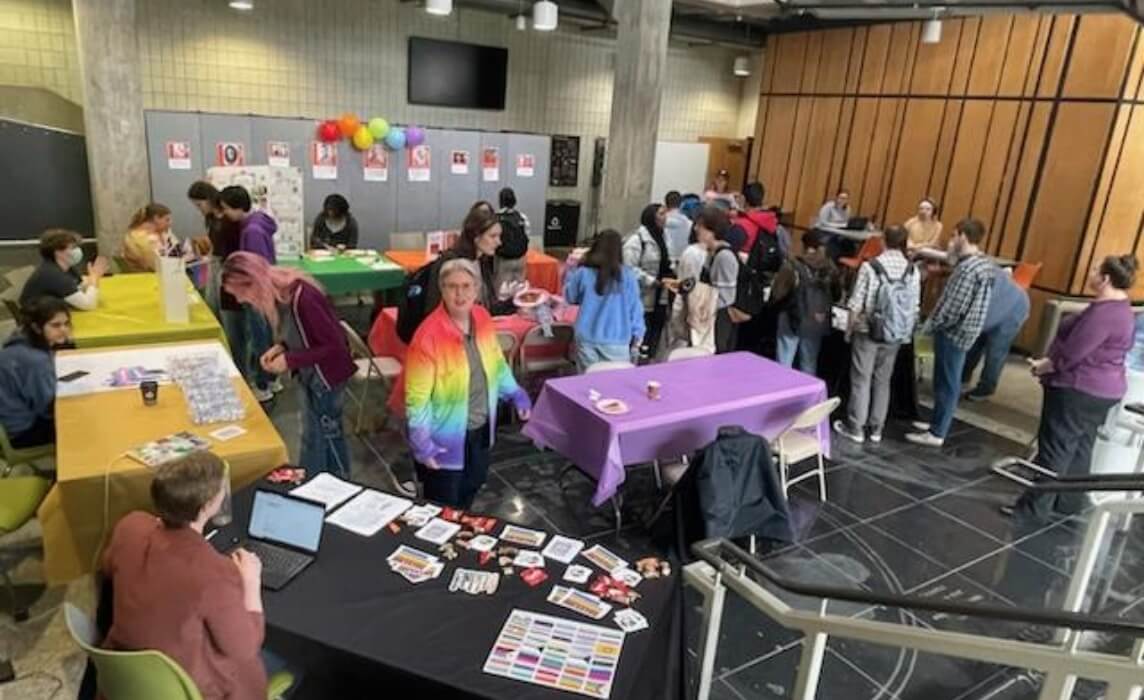 Several colorful booths set up in the atrium of the College of Science, with dozens of people visiting the booths.