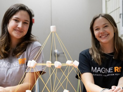 two students behind a marshmallow spaghetti tower