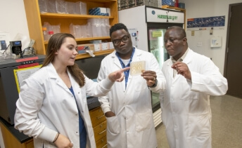 An R I T student researcher, pointing out results to André Hudson and Bolaji Thomas.