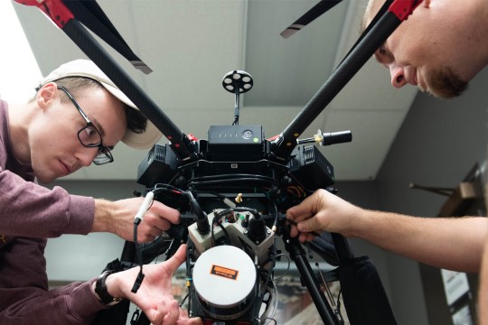 two students making adjustments to a drone.