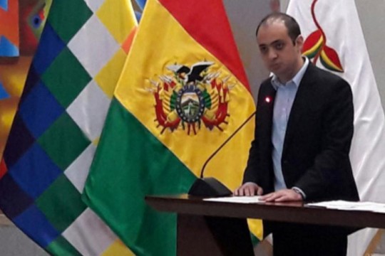 man speaking at podium next to the Bolivian flag.