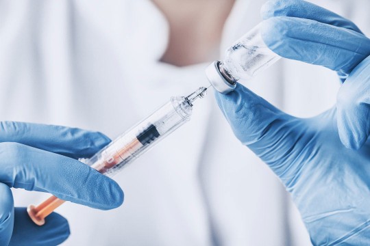two hands in blue gloves hold a vaccine in a needle