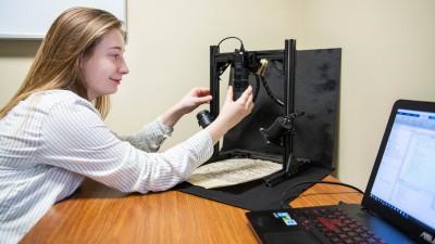 student adjusts cameras pointing to a manuscript next to a laptop.