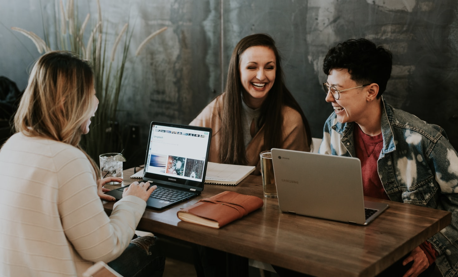 three people at a table laughing and discussing with laptops in front of them