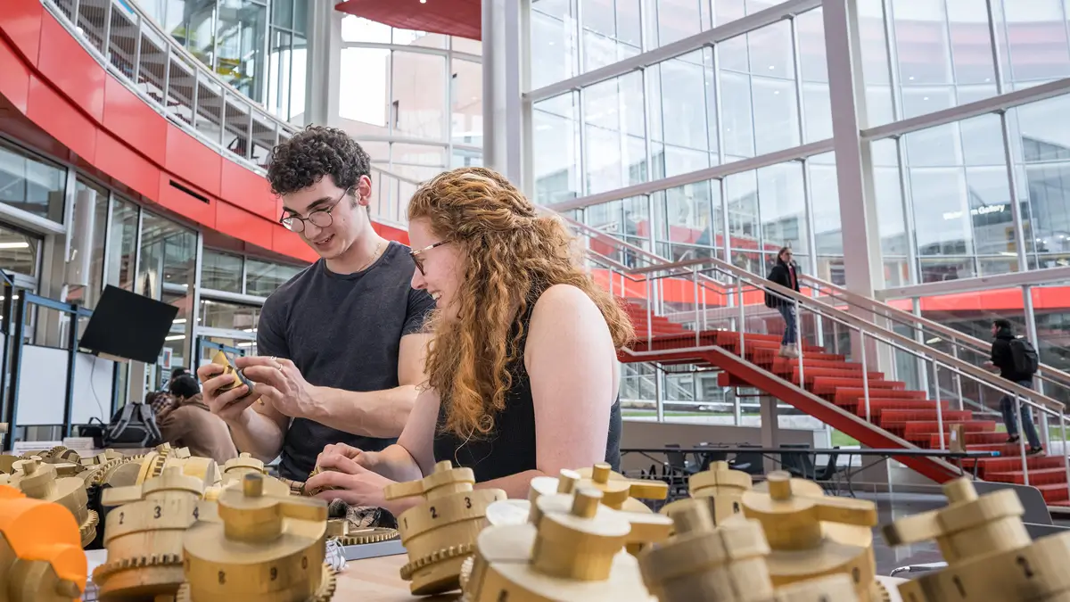 Two people looking at a table of 3D printed parts in the Atrium of the SHED.
