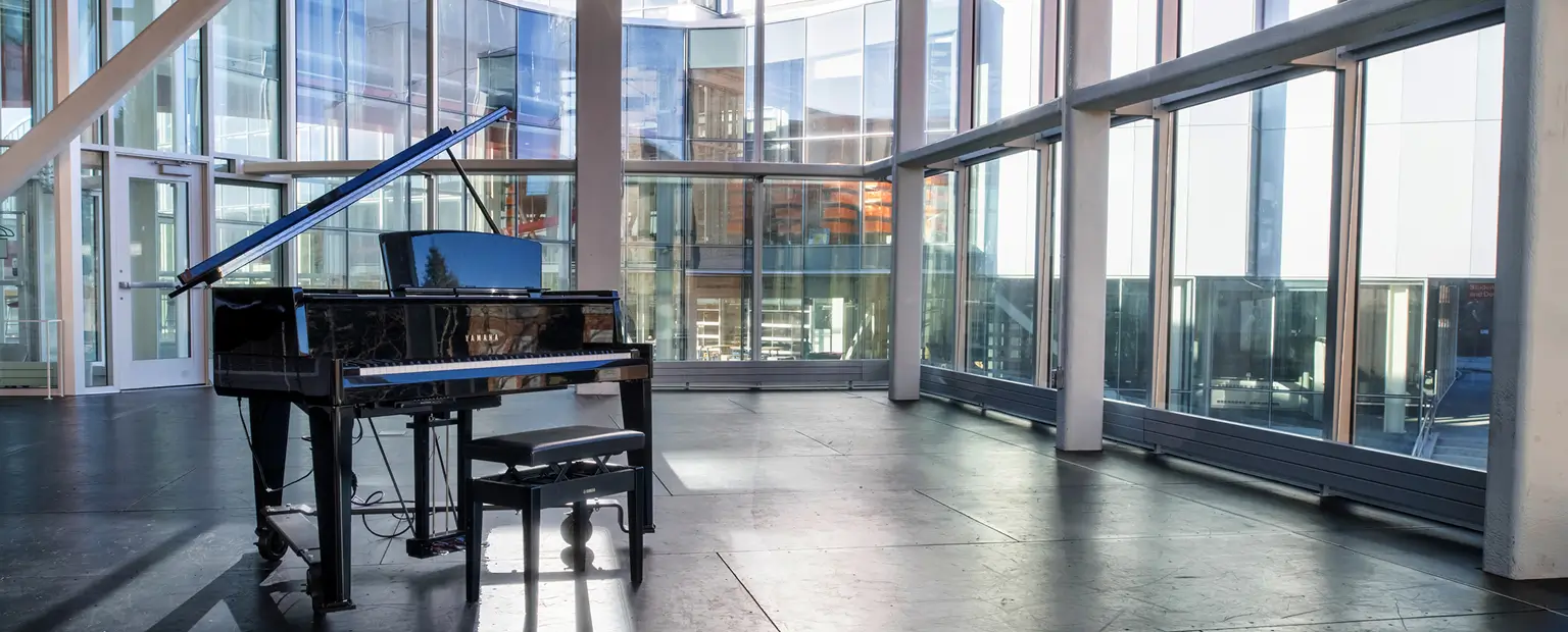 A piano sitting in front of a wall of windows in the SHED.