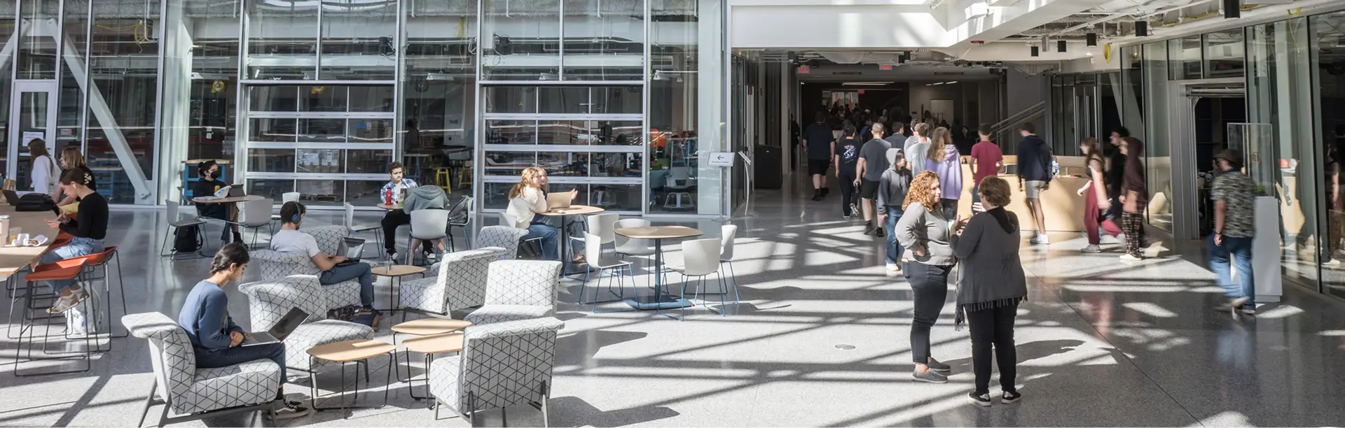 An interior view of the main lobby of the SHED, showing people walking through and some sitting in available chairs.