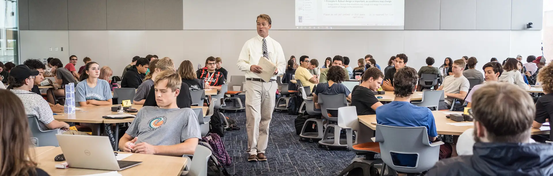 A professor walks between tables of students during a class.