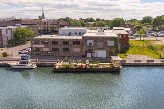 A floating riverside pavilion sits along the canal beside downtown buildings.