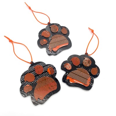 Three orange and black ornaments in the shape of a paw made of cut circuit board hung on an orange string.