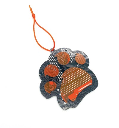 A single orange and black ornament in the shape of a paw made of cut circuit board hung on an orange string.