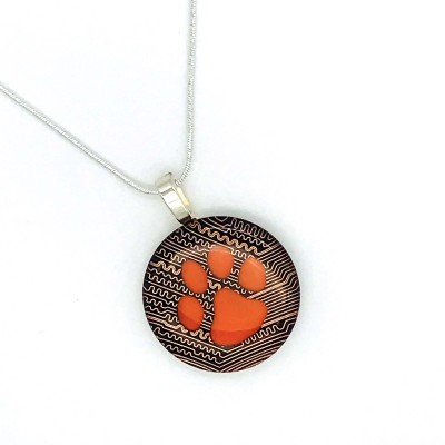 Round pendant made of circuit board with an orange paw in the center on a silver chain.
