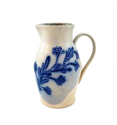 A white ceramic pitcher with a blue illustration of a vine across the front.