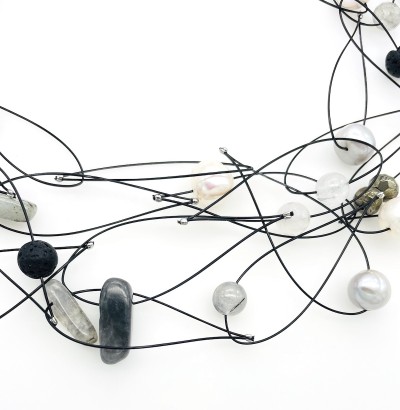 close up of a variety of faceted beads, shells, naturally tumbled glass, and semi precious stones on a black coated wire necklace.