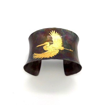 A wide copper cuff bracelet with a gold illustration of a heron in flight.