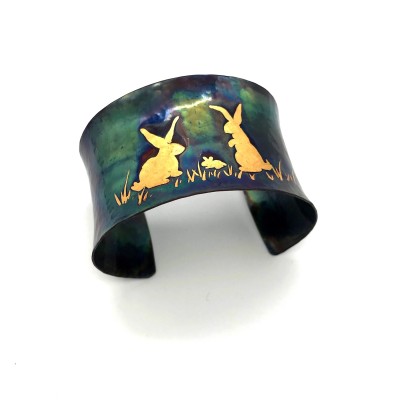 A wide copper cuff bracelet with a gold illustration of two bunny rabbits.