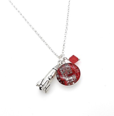 A red pendant with a circuit board design and silver rocket charm and red diamond shaped bead on a silver chain.