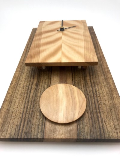 looking up at Rectangular clock with dark body and light face with short pendulum made from wood.