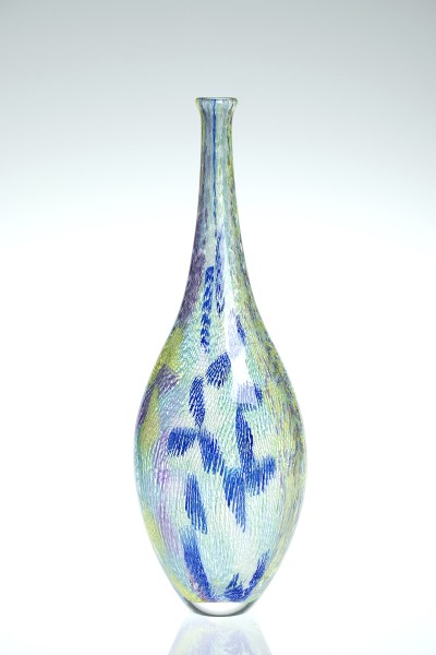 a tall narrow glass bottle form with a clear glass base and multi colored hatching of green and blue forming a pin wheel pattern in places.
