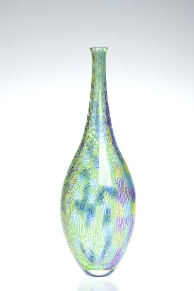 a tall narrow glass bottle form with a clear glass base and multi colored hatching of green and blue forming a pin wheel pattern in places.