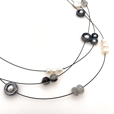 a necklace of a long thin cable that is strung randomly with beads in variety of shape and color and materials from clay to white pearls to faceted glass.