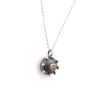 a handmade pendant made of silver in a dome shape with a yellow stone in the center.