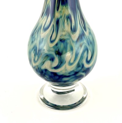 a hand blown teardrop shaped glass vase with a stormy swirl pattern of blues and greys across the surface with a clear glass foot.