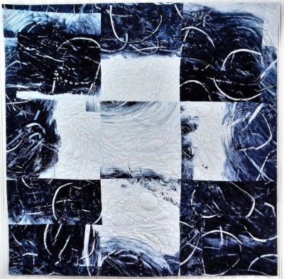 a painterly fabric quilt with an overriding nine box grid that resembles a tic tac toe board in blues and whites.