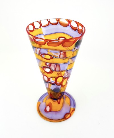 a glass footed cup with a complex pattern of layered, swirly bands of transluscent colors from orange to circles of red and bands of purple.