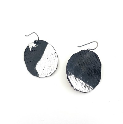 a pair of earrings made of a circular piece of canvas an painted with swatch of black pigment.