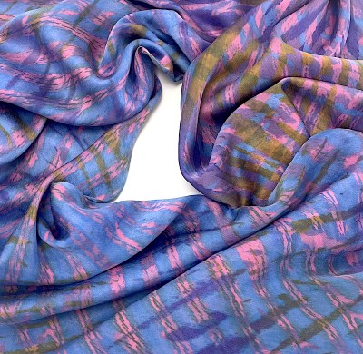 a close up of a multi color silk scarf with pink, purple and blue criss cross design arranged in a circle.