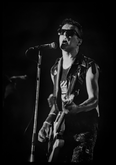 a black and white photograph of musician Joe Strummer playing a guitar of stage.