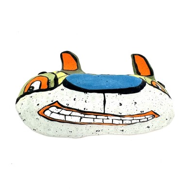 a hand sculpted ceramic mask form of a wide cat like face with orange ears, a blue nose, and a toothy smile.
