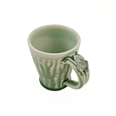Angled view of soft green glazed mug adorned with a small bat