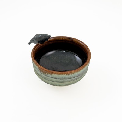 Small bowl with green hues and a brown interior, with a small black crow on the rim