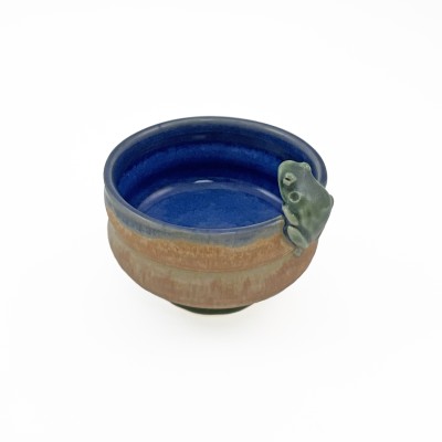 Small bowl with a tan-orange exterior, with a deep blue interior glaze and a tiny frog perched on the rim