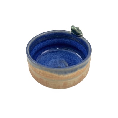 Turned view of small bowl with a tan-orange exterior, with a deep blue interior glaze and a tiny frog perched on the rim