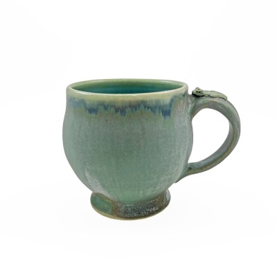 Angled view of soft green glazed mug adorned with a small frog