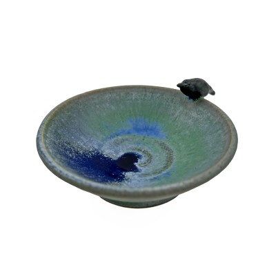 Small bowl with green hues and blue accents inside, with a small black crow on the rim