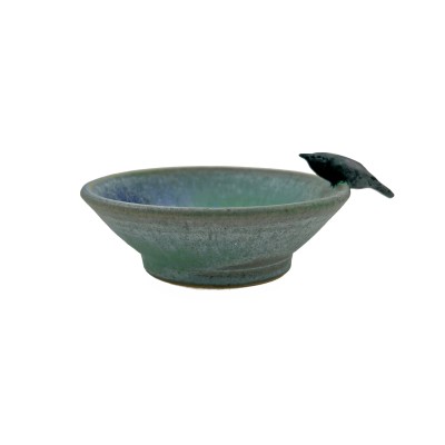 Side view of small bowl with green hues and blue accents inside, with a small black crow on the rim