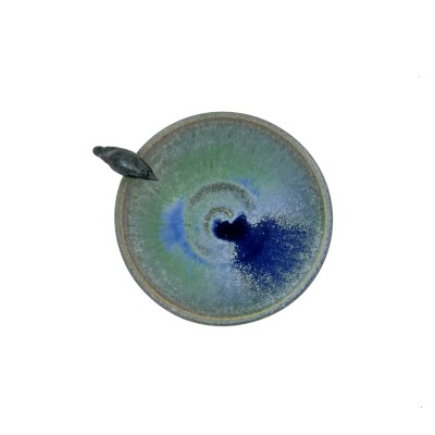 Top  view of small bowl with green hues and blue accents inside, with a small black crow on the rim