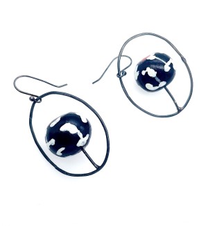 A pair of earrings with a cage like circle around a central clay bead, the bead is black with white spots.