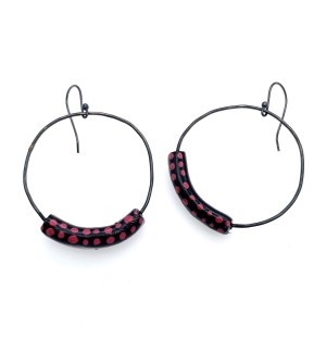 A pair of earrings shaped like a large circle with a section of the circle replaced with a black clay arch with red dots.