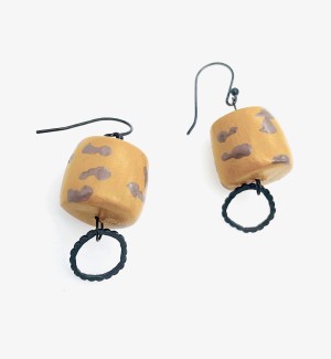 A pair of earrings with a mustard yellow cylinder with grey spots, a small open loop hangs below.