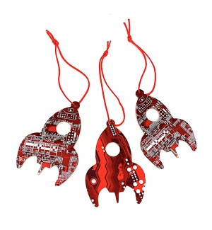 Three red rocket shaped ornaments made of circuit board with a cut circle window in the center hung with red string.