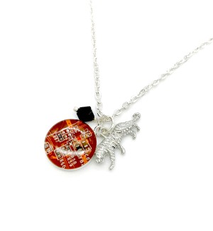 An orange pendant with a circuit board design and silver tiger charm and a black diamond shaped bead on a silver chain.