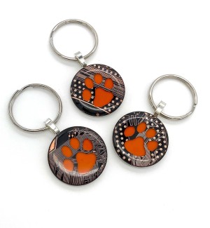Three round keychains made of circuit board with an orange paw in the center.
