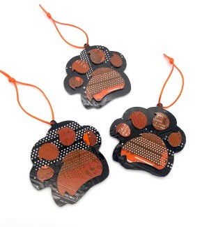 Three orange and black ornaments in the shape of a paw made of cut circuit board hung on an orange string.