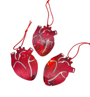 Three red ornaments shaped like anatomical interpretations of a heart made of circuit board hung with red string.